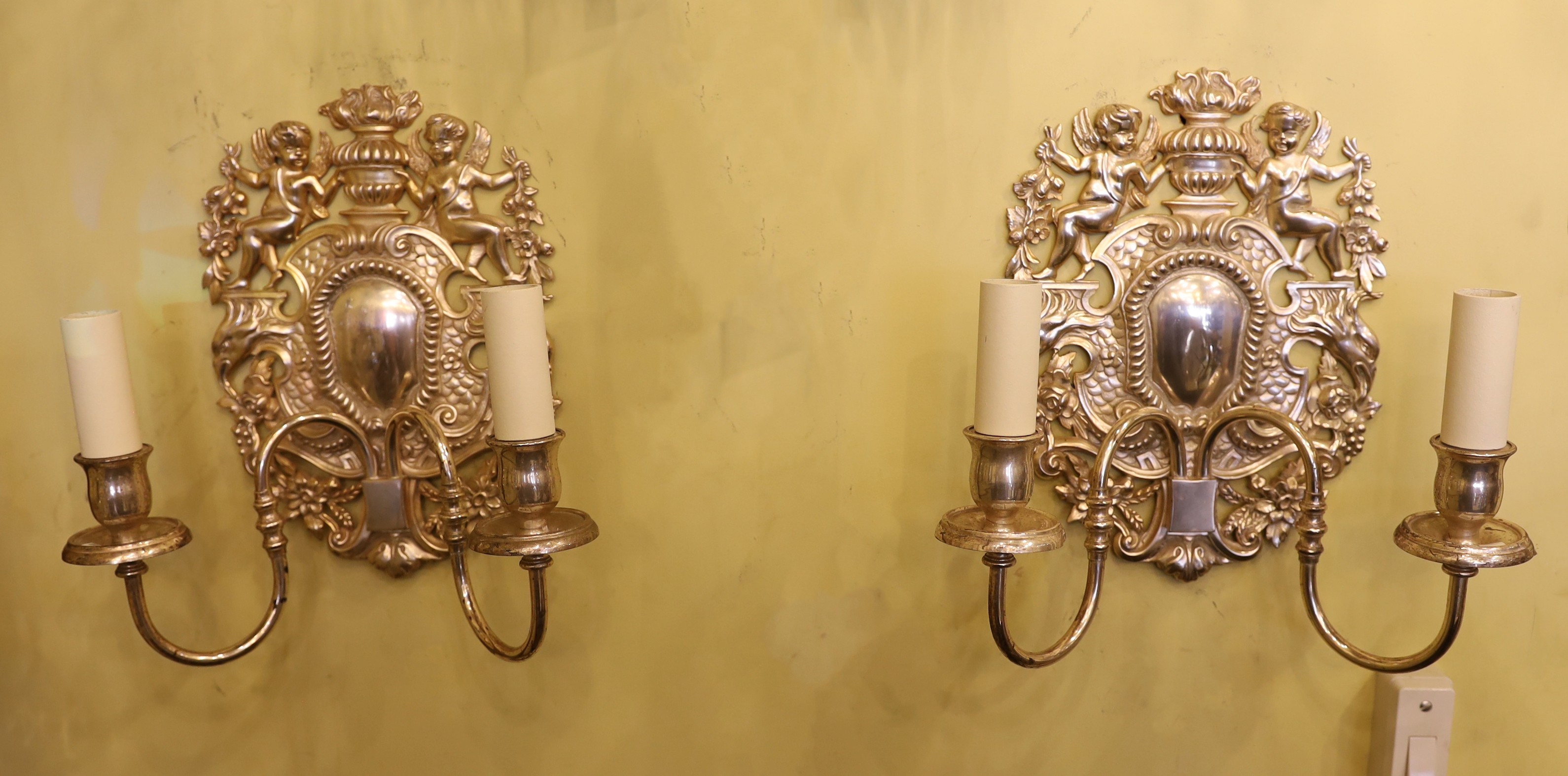 A pair of 17th century style silver plated wall lights with cherub and flower back plates and scroll and branches, height 30cm